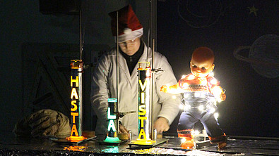 Chemiemitarbeiter mit Weihnachtsmütze steht am Experimentiertisch. Vor ihm stehen drei Raketen mit der Aufschrift: Hasta la vista.