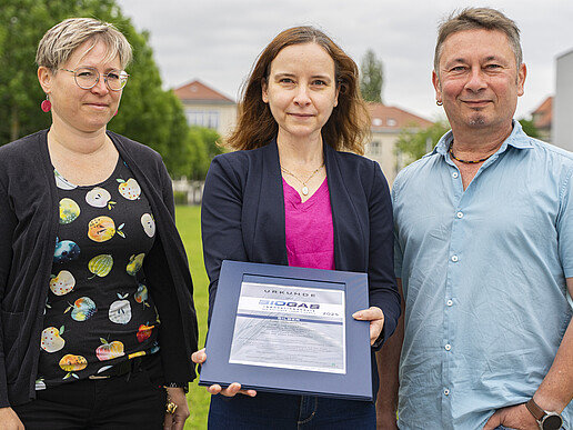 Frau Dr. Marzena Poraj-Kobielska, Frau Dr. Judit Harsányi und Herr Dipl.-Ing. Matthias Tirsch stehen auf einer Wiese auf der Zittauer Campusachse. Frau Dr. Harsanyi hält die Urkunde in den Händen.