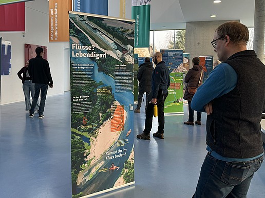 Ein Besucher steht vor einem Roll-up im Foyer von Haus Z Vier, umgeben von anderen Besuchenden der Ausstellung.