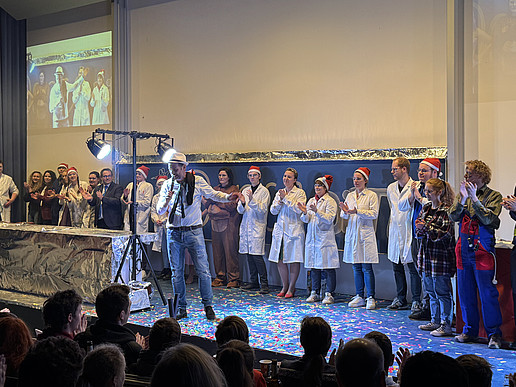 Das Schauvorlesungsteam steht in einer Reihe auf dem Vorlesungssaal-Podium und klatscht Beifall.