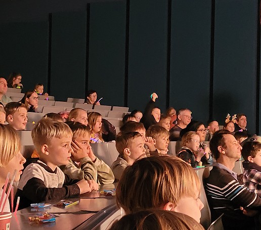 Kinder sitzen auf Sitzreihen im Audimax und schauen in Richtung Bühne.