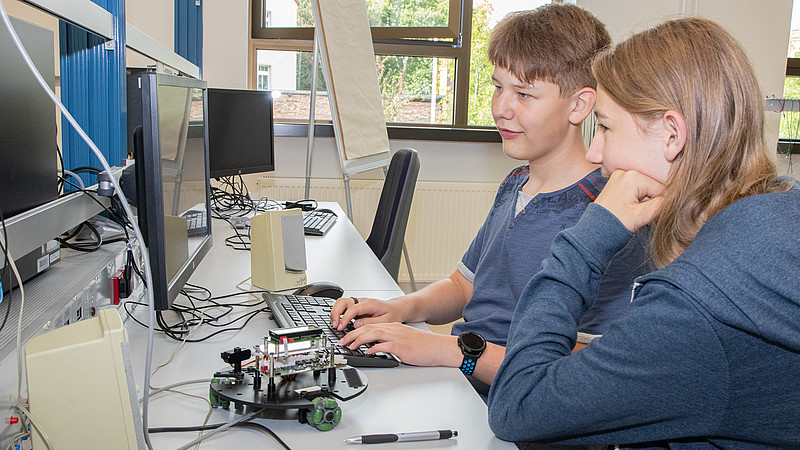 Zwei Schüler sitzen am Labortisch und programmieren einen Roboter.