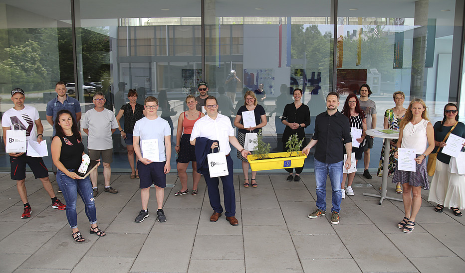 Foto: Jens Freudenberg Eine große Gruppe von Schrittzähler-Challenge-Teilnehmenden steht vor Haus 4 und lächelt in die Kamera. Die Ausgezeichneten halten ihre Urkunden in die Kamera.