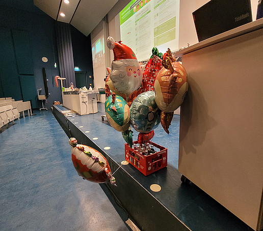 Ein Limoflaschen-Kasten mit angebundenen Luftballons steht auf der Bühne im Audimax.