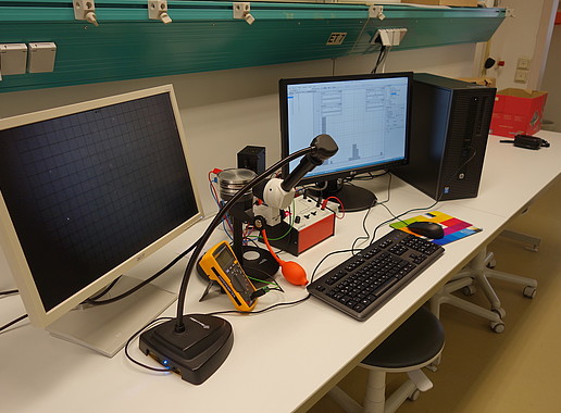 Laborarbeitsplatz mit Monitoren, Computer und anderen Geräten für das physikalische Praktikum