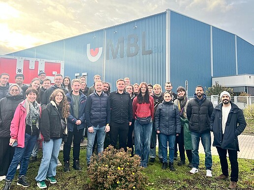 Eine Gruppe Studierender steht auf dem Firmengelände einer Fabrik.