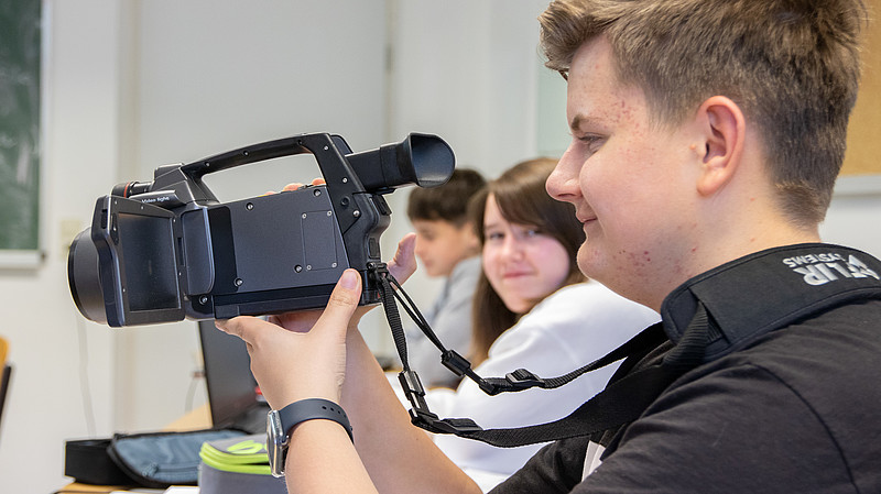 Ein Schüler hält eine Wärmebildkamera in der Hand und schaut durch das Objektiv.