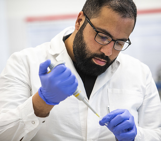 Ezzat im Labor mit blauen Handschuhen und einer Pipette in den Händen.