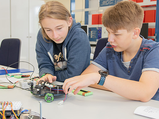 Zwei Schüler sitzen an einem Labortisch und befassen sich mit dem Aufbau eines Roboters.