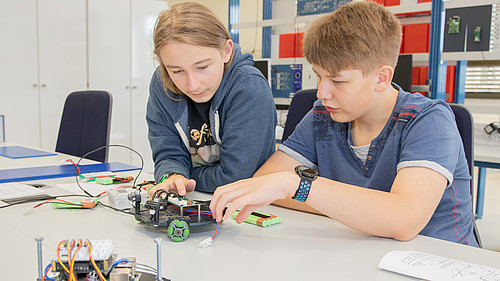Zwei Schüler sitzen an einem Labortisch und befassen sich mit dem Aufbau eines Roboters.
