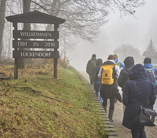 Eine Wandertruppe auf dem Weg ins Gebirge geht eine Straße entlang.