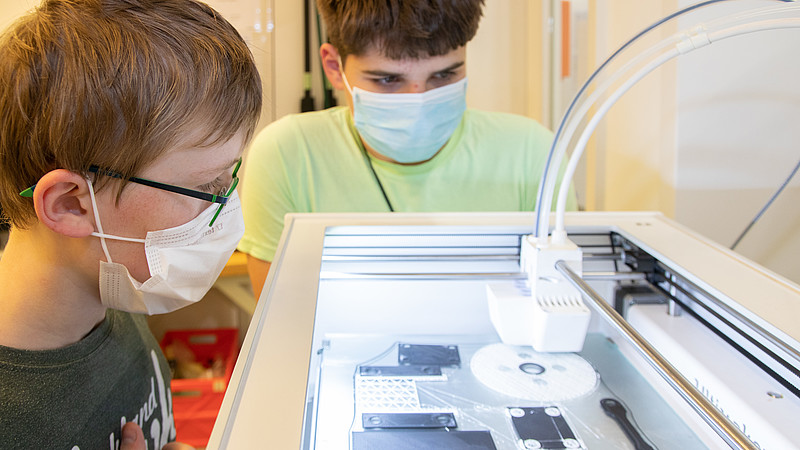 Zwei Schüler beobachten, wie ein 3D-Drucker arbeitet.