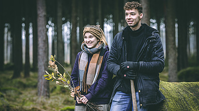 Zwei Studierende stehen lächeln im Wald.