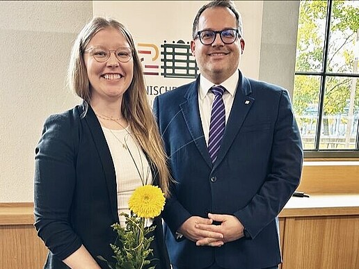 Professorin Schellhammer steht neben Rektor Kratzsch und hält eine gelbe Blume in der Hand, beide lächeln in die Kamera.